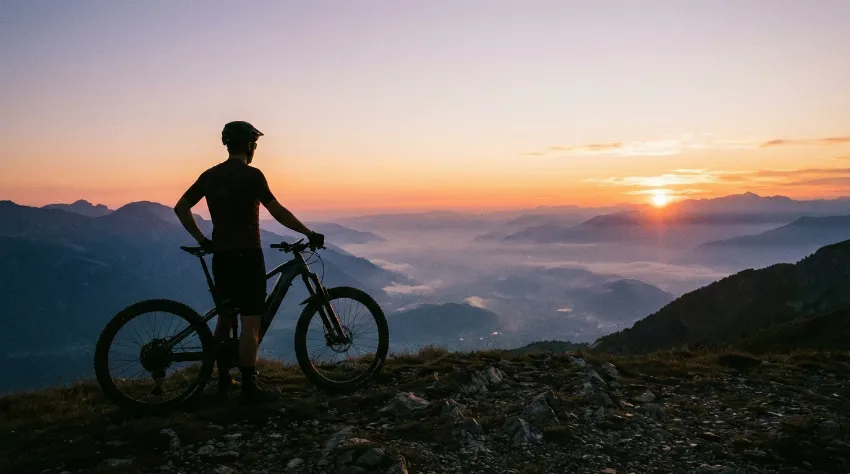 Kolesar na vrhu gore ob sončnem zahodu uživa v razgledu